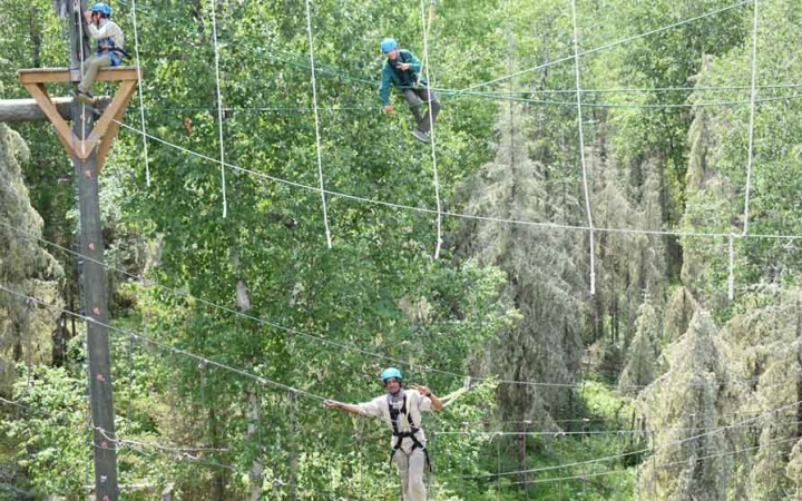 two students are suspended by ropes as they make their way through a ropes course on an outward bound course